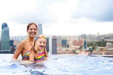 Çocuklar Singapur 'da aile tatilinde çatıda yüzüyorlar. Lüks oteldeki sonsuz havuzdan şehrin silüeti. Çocuklar Asya 'da yüzer ve gökdelen manzarasının tadını çıkarırlar. Küçük çocukla seyahat et..