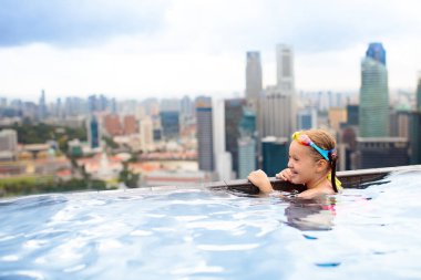 Çocuklar Singapur 'da aile tatilinde çatıda yüzüyorlar. Lüks oteldeki sonsuz havuzdan şehrin silüeti. Çocuklar Asya 'da yüzer ve gökdelen manzarasının tadını çıkarırlar. Küçük çocukla seyahat et..