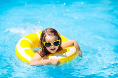 Havuzda yüzen çocuk şişme sarı limon halkası takıyor. Küçük kız turuncu yüzgeçle yüzmeyi öğreniyor. Bebek ve bebek için su oyuncağı. Çocuklar için sağlıklı bir açık hava sporu. Çocuklar plaj eğlencesi.  