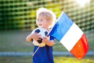 Çocuklar dışarıda futbol oynarlar. Ulusal bayrağı olan Fransa takımı taraftarları. Çocuklar futbol maçında gol attılar. Fransız formalı ve kramponlu çocuk topa vuruyor. Taraftarlar sahada zaferi kutluyor.