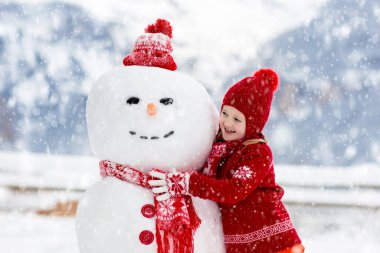 Kardan adam yapan çocuk. Çocuklar kardan adam yapar. Erkek ve kız, karlı kış gününde dışarıda oynuyorlar. Noel tatilinde dağlarda aile eğlencesi. Çocuklar İsviçre dağ manzarasında oynuyorlar..