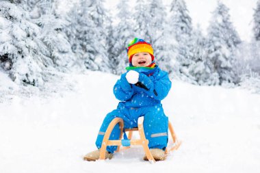 Küçük çocuk kızakla gezintiye çıkıyor. Çocuk kayağı. Kızak süren küçük bir çocuk. Çocuklar karda dışarıda oynarlar. Çocuklar kışın Alp dağlarında kızak kullanırdı. Aile Noel tatili için açık hava eğlencesi.