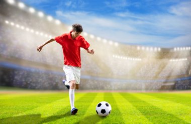 Stadyum sahasında futbolcu. Futbol maçı. Kırmızı tişörtlü ve beyaz şortlu genç adam dışarıda topa vuruyor. Koşan ve zıplayan bir sporcu. Şampiyonluk maçı zaferi.