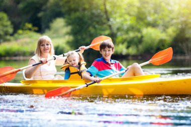 Kano üzerinde kürek çeken çocuk. Çocuklar için yaz kampı. Ailemle kano ve kano gezisi. Kanodaki çocuklar. Aile kano gezisinde. Yaz tatilinde vahşi doğa ve su eğlencesi. Kamp ve balıkçılık.