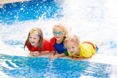 Çocuklar yüzme havuzunda oynar. Çocuklar aile yaz tatili tropikal resort açık yüzme havuzunda yüzmeyi öğrenmek. Su ve splash eğlenmek için tatil genç çocuk. Çocuk ve bebek için güneş koruma.
