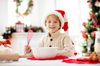 Aile Noel kurabiyesi pişiriyor. Büyükanne ve çocuk zencefilli kek pişirir. Çocuklar Xmas eğlencesi. Noel Baba şapkalı küçük çocuk kış kurabiyesi için hamur yapıyor. Ev tatili dekorasyonu.