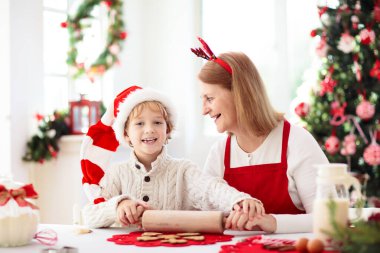 Aile Noel kurabiyesi pişiriyor. Büyükanne ve çocuk zencefilli kek pişirir. Çocuklar Xmas eğlencesi. Noel Baba şapkalı küçük çocuk kış kurabiyesi için hamur yapıyor. Ev tatili dekorasyonu.