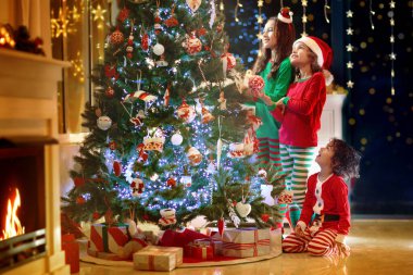 Noel arifesinde Noel ağacı ve şömine başında çocuklar. Noel 'i evde kutlayan çocuklu bir aile. Erkek ve kız aynı pijamaları giyip Noel ağacını süslüyor ve hediyeleri açıyor. Çocuklar için tatil hediyeleri.