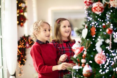 Evde Noel ağacı süsleyen çocuk. Xmas süsü takmış küçük bir kız ve oğlan. Çocuklu aile kış tatilini kutlar. Çocuklar Noel için oturma odasını ve şömineyi dekore ederler.. 