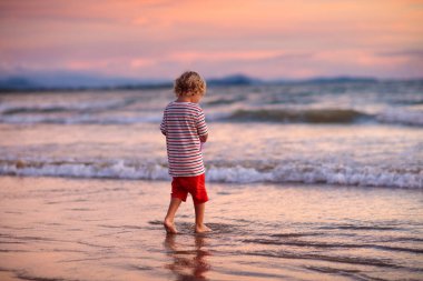 Okyanus sahilinde oynayan çocuk. Gün batımında dalgalara atlayan çocuk. Çocuklu aile için deniz tatili. Yaz tatili sırasında egzotik adanın tropik plajda çalışan küçük çocuk. 