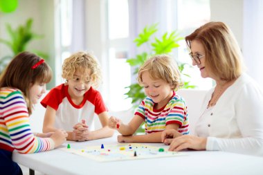 Aile evde masa oyunu oynuyor. Çocuklar stratejik oyunlar oynar. Küçük çocuk zar atıyor. Yaz tatili için eğlenceli bir ev aktivitesi. Kardeşler arası bağ. Eğitici oyuncaklar. Arkadaşlar oyun gecesinin tadını çıkarın.