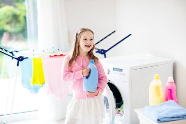 Çocuk Çamaşırhane, çamaşır makinesi ile Oda veya kurutma. Çocuk ile aile işleri yardımcı. Modern ev aygıtları ve çamaşır deterjan beyaz güneşli evinde. Raf kurutma üzerinde temiz yıkanmış kıyafetler. 
