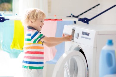 Çocuk Çamaşırhane, çamaşır makinesi ile Oda veya kurutma. Çocuk ile aile işleri yardımcı. Modern ev aygıtları ve çamaşır deterjan beyaz güneşli evinde. Raf kurutma üzerinde temiz yıkanmış kıyafetler. 
