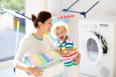 Anne ve çocuklar Çamaşırhane, çamaşır makinesi ile Oda veya kurutma. Aile işleri. Modern ev aygıtları ve çamaşır deterjan beyaz güneşli evinde. Raf kurutma üzerinde temiz yıkanmış kıyafetler. 
