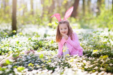Bahar bahçesinde Paskalya yumurtası avı. Çiçek tarlasında saklı renkli yumurta ve şeker arayan çocuklar. Tavşan kulaklı ve yumurta sepetli çocuklar. Aile Paskalya kutlaması. Oynayan kız.