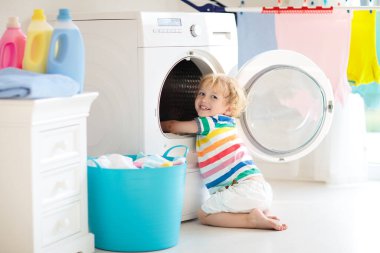 Çocuk Çamaşırhane, çamaşır makinesi ile Oda veya kurutma. Çocuk ile aile işleri yardımcı. Modern ev aygıtları ve çamaşır deterjan beyaz güneşli evinde. Raf kurutma üzerinde temiz yıkanmış kıyafetler. 