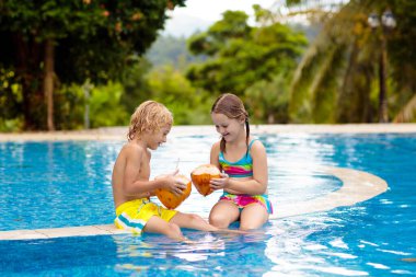 Açık havuzda hindistan cevizi içen çocuk. Çocuklar tropik tatil köylerinde yüzerler. Çocuklar için sağlıklı egzotik meyve ferahlatıcı. Genç bir çocukla seyahat et. Kumsal ve su eğlencesi. Yaz aile tatili.