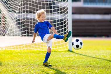 Çocuklar stadyum sahasında futbol oynarlar. Çocuklar futbol maçında gol atıyor. Küçük çocuk topa vuruyor. Okul spor kulübü. Genç oyuncu için alıştırma.