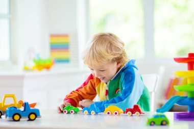 Küçük çocuk oyuncak araba oynuyor. Renkli eğitim aracı ve ulaşım oyuncakları olan genç bir çocuk. Çocuk arabasını Rainbow otoparkına sürüyor. Evde ya da kreşte çocuklar. Anaokulu ya da anaokulu oyunu.