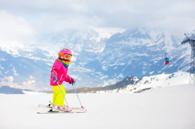 Çocuk dağlarda kayak yapıyor. Güvenlik kaskı, gözlüğü ve direkleri olan aktif bir çocuk. Küçük çocuklar için kayak yarışı. Aile için kış sporu. Alp okulunda çocuklar kayak dersi alıyor. Küçük kayakçı karda yarışıyor
