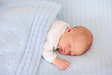 Yeni doğan bebek yatakta. Yeni doğan çocuk mavi örgü battaniye altında uyuyor. Çocuk uyku. Çocuklar için yatak takımları. Bebek yatakta uyuyor. Sağlıklı çocuk doğumdan kısa bir süre sonra. Kablo Tekstil Örme.