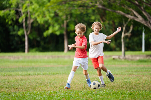 Ребенок играет в футбол. Дети играют в футбол на открытом поле. Мальчик пинает мяч в летнем парке. Здоровый образ жизни для маленьких детей. Школьный спортивный клуб. Юниорская лига.