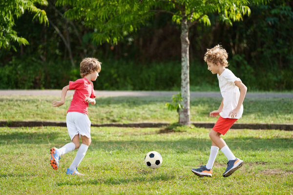 Ребенок играет в футбол. Дети играют в футбол на открытом поле. Мальчик пинает мяч в летнем парке. Здоровый образ жизни для маленьких детей. Школьный спортивный клуб. Юниорская лига.