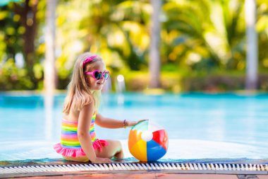 Havuzda şişme oyuncak topu olan bir çocuk. Çocuklar yüzer. Genç çocuklar için renkli gökkuşağı yüzüyor. Küçük kız yaz tatilinde tropikal tatil köyünde eğleniyor. Kumsal ve su eğlencesi. 