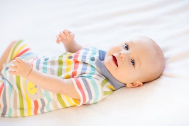 Beyaz güneşli yatak odasında sevimli bir bebek. Yeni doğmuş çocuk yatakta dinleniyor. Küçük çocuklar için çocuk odası. Çocuklar için tekstil ve yatak. Aile sabahı evde. Oyuncak ayıyla karnını doyururken doğan yeni çocuk..