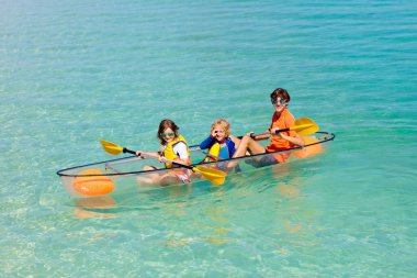 Çocuklar okyanusta kayak yapıyor. Tropikal denizde kanodaki çocuklar. Genç bir çocukla aktif tatil. Ebeveynler, küçük bir oğlan ve güzel bir sahilde kanodaki bir kız. Çocukla birlikte tatil aktivitesi. Aile suyu eğlencesi.