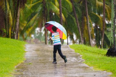 Sonbahar yağmurunda oynayan çocuk. Parktaki çamurlu su birikintisine atlayan çocuk. Şiddetli sonbahar yağmuru altında renkli şemsiyeli küçük bir çocuk. Fırtınalı yağmurlu hava eğlencesi.