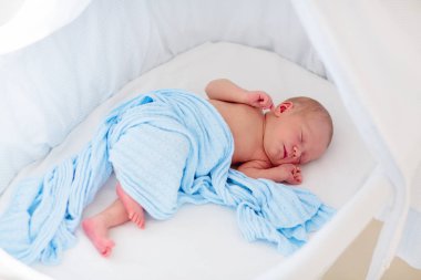 Beyaz güneşli yatak odasında sevimli bir bebek. Yeni doğmuş çocuk yatakta dinleniyor. Küçük çocuklar için çocuk odası. Çocuklar için tekstil ve yatak. Aile sabahı evde. Oyuncak ayıyla karnını doyururken doğan yeni çocuk..