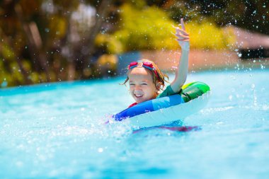 Yüzme havuzunda yüzen bir çocuk. Çocuklar yüzer. Genç çocuklar için renkli gökkuşağı yüzüyor. Küçük çocuk yaz tatilinde tropik tatil köyünde eğleniyor. Plaj ve su oyuncakları. Güneş koruması.