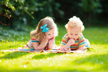 Çocuklar güneşli yaz bahçesinde dışarıda oynarlar. Çocuk güzel bir parkta battaniyede kitap okuyor. Çocuklarla piknik. Bebekle yaz tatili için eğlenceli aktiviteler.