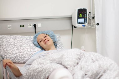 Modern hastanenin ameliyat sonrası bakım odasında iyileşmekte olan genç bir hasta. Diz travması sonrası alçı ve nabız ölçer olan kadın ortopedi kliniğinin dinlenme odasında izleniyor..