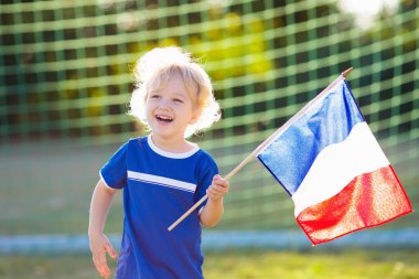 Çocuklar dışarıda futbol oynarlar. Ulusal bayrağı olan Fransa takımı taraftarları. Çocuklar futbol maçında gol attılar. Fransız formalı ve kramponlu çocuk topa vuruyor. Taraftarlar sahada zaferi kutluyor.