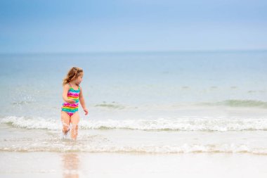 Tropik plajda oynayan çocuklar. Çocuklar yaz tatilinde yüzer ve denizde oynarlar. Kum ve su eğlencesi, küçük çocuklar için güneş koruması. Küçük bebek okyanus kıyısında koşuyor ve zıplıyor.