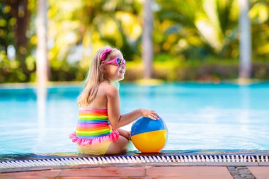 Havuzda şişme oyuncak topu olan bir çocuk. Çocuklar yüzer. Genç çocuklar için renkli gökkuşağı yüzüyor. Küçük kız yaz tatilinde tropikal tatil köyünde eğleniyor. Kumsal ve su eğlencesi. 