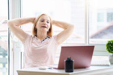Dizüstü bilgisayarı ve cep telefonu olan bir kadın. Güneşli modern ofiste çalışan güzel, mutlu bir kadın. İşyerinde serbest çalışan biri. Emeklilik yaşı eğitimi. Online alışveriş ve bankacılık.