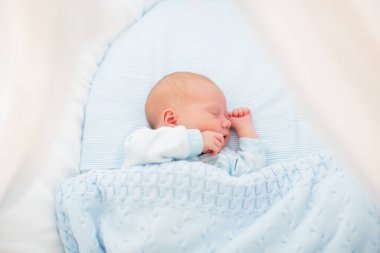 Yeni doğan bebek yatakta. Yeni doğan çocuk mavi örgü battaniye altında uyuyor. Çocuk uyku. Çocuklar için yatak takımları. Bebek yatakta uyuyor. Sağlıklı çocuk doğumdan kısa bir süre sonra. Kablo Tekstil Örme.