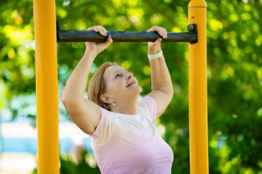 Egzersiz yapan yaşlı kadın. Yaz şehrindeki güneşli stadyumda koşan formda bir bayan. Emeklilik yaşında spor. Aktif bir bayan, dışarıda sağlıklı bir antrenmandan sonra geriniyor. Emekli kişi için spor.
