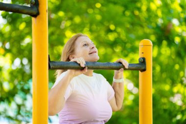 Egzersiz yapan yaşlı kadın. Yaz şehrindeki güneşli stadyumda koşan formda bir bayan. Emeklilik yaşında spor. Aktif bir bayan, dışarıda sağlıklı bir antrenmandan sonra geriniyor. Emekli kişi için spor.