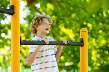 Çocuk parkında. Okul bahçesinde egzersiz yapan aktif bir çocuk. Çocuklar oynar ve tırmanır. Maymun parmaklıklarında küçük bir çocuk. Çocuklar güneşli yaz gününde güzel parkta eğleniyorlar..