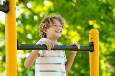 Çocuk parkında. Okul bahçesinde egzersiz yapan aktif bir çocuk. Çocuklar oynar ve tırmanır. Maymun parmaklıklarında küçük bir çocuk. Çocuklar güneşli yaz gününde güzel parkta eğleniyorlar..