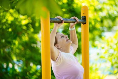 Egzersiz yapan yaşlı kadın. Yaz şehrindeki güneşli stadyumda koşan formda bir bayan. Emeklilik yaşında spor. Aktif bir bayan, dışarıda sağlıklı bir antrenmandan sonra geriniyor. Emekli kişi için spor.