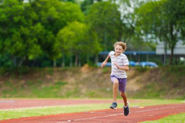 Çocuklar uzun atlama sporları eğitimi alıyor. Okul stadyumunda kum havuzuna atlayan bir çocuk. Çocuklar için sağlıklı bir açık hava egzersizi. Spor yapan genç bir sporcu. Genç çocuk için spor.