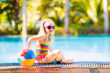 Havuzda şişme oyuncak topu olan bir çocuk. Çocuklar yüzer. Genç çocuklar için renkli gökkuşağı yüzüyor. Küçük kız yaz tatilinde tropikal tatil köyünde eğleniyor. Kumsal ve su eğlencesi. 