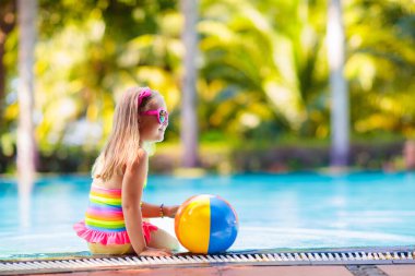 Havuzda şişme oyuncak topu olan bir çocuk. Çocuklar yüzer. Genç çocuklar için renkli gökkuşağı yüzüyor. Küçük kız yaz tatilinde tropikal tatil köyünde eğleniyor. Kumsal ve su eğlencesi. 