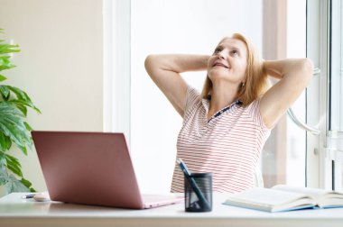 Dizüstü bilgisayarı ve cep telefonu olan bir kadın. Güneşli modern ofiste çalışan güzel, mutlu bir kadın. İşyerinde serbest çalışan biri. Emeklilik yaşı eğitimi. Online alışveriş ve bankacılık.