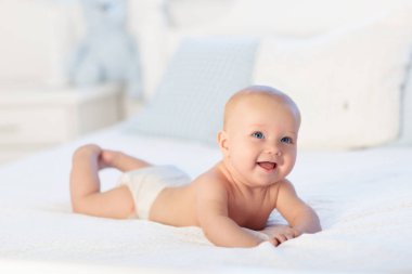 Erkek bebek bezi beyaz güneşli yatak odasında. Yeni doğan çocuk yatakta rahatlatıcı. Kreş çocuklar için. Tekstil ve çocuklar için yatak. Aile sabah evde. Oyuncak ayı ile mide süre içinde yeni doğmuş çocuk.